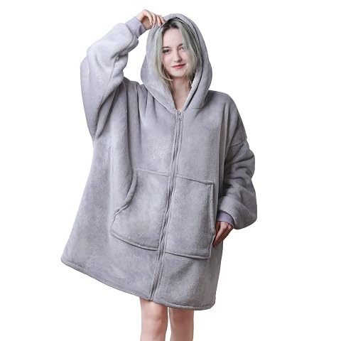 Poncho d’intérieur gris à capuche et fermeture zippée, avec doublure sherpa visible dans une chambre calme.