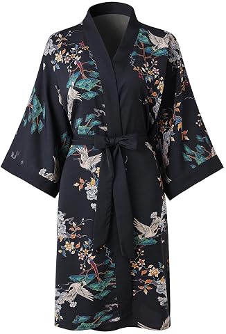 Peignoir kimono noir à motif floral, ceinture nouée et poches, posé dans une chambre au linge crème.