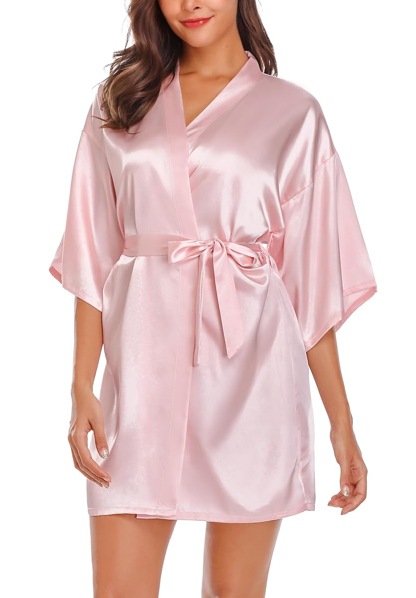 Peignoir kimono rose uni avec col en V oblique, manches amples et ceinture nouée sur un lit.