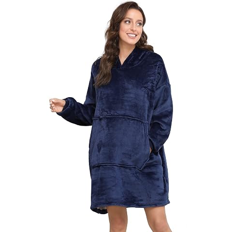 Poncho d’intérieur bleu uni à capuche et grande poche, posé sur un fauteuil en bois dans une chambre calme.