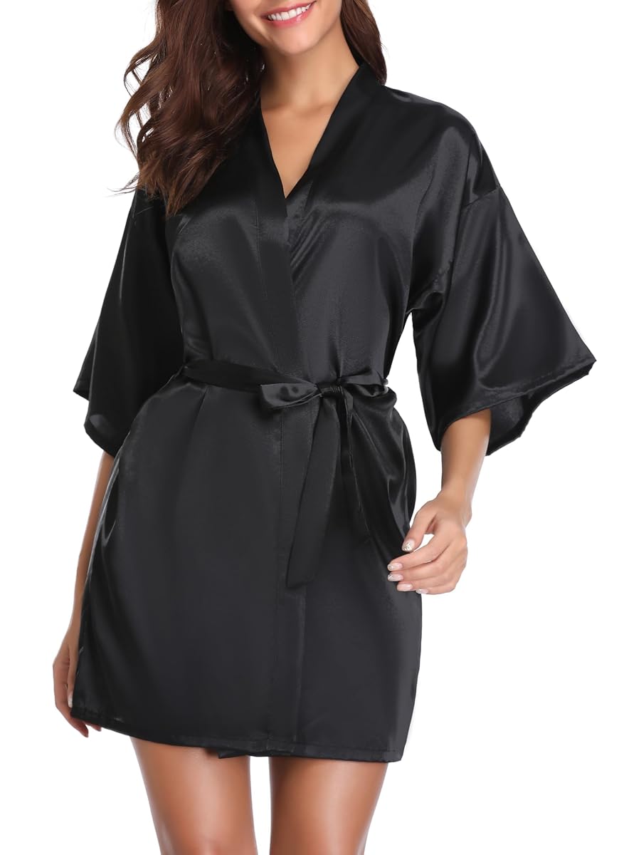 Kimono court noir en satin posé sur un lit dans une chambre calme à la lumière douce.