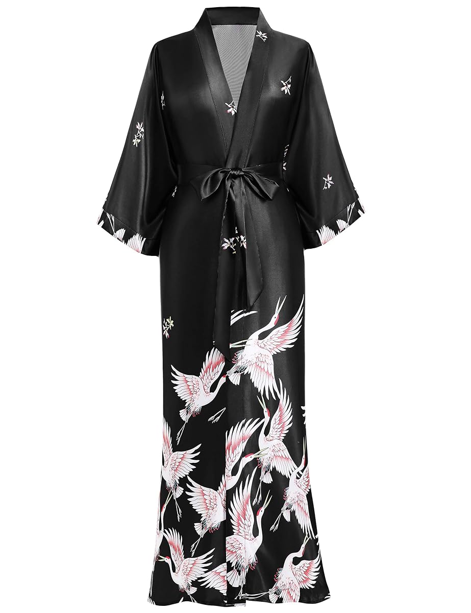 Kimono long en satin noir à motif de grues, posé sur un lit dans une chambre à la lumière douce.
