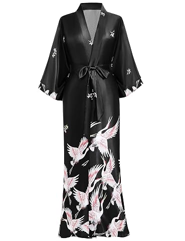 Kimono long en satin noir à motif de grues, posé sur un lit dans une chambre à la lumière douce.