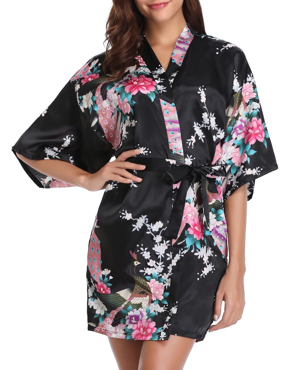 Kimono court en satin noir à motif floral de paon, posé sur un lit aux draps crème