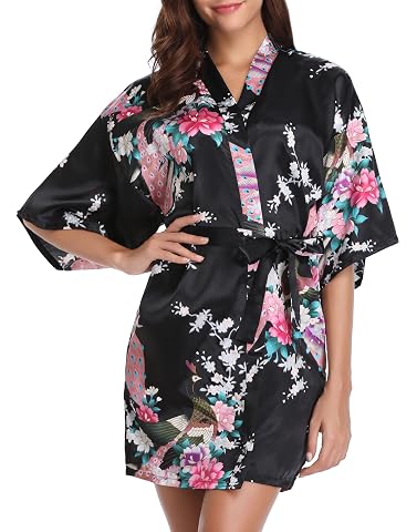 Kimono court en satin noir à motif floral de paon, posé sur un lit aux draps crème